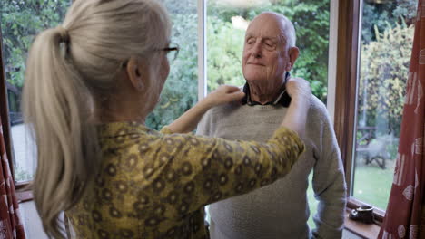 elderly woman helping older man with his shirt