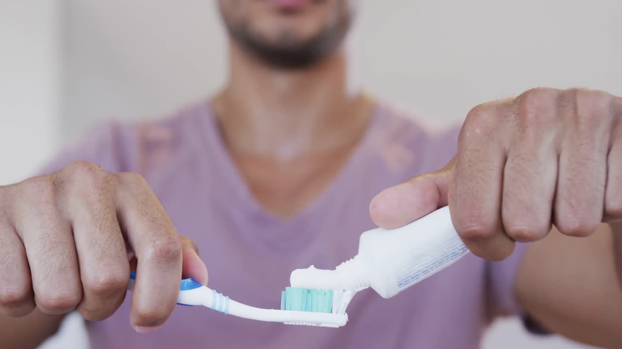 Close up of biracial man of biracial man applying toothpaste to toothbrush in bathroom, slow motion