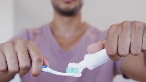 close up of biracial man of biracial man applying toothpaste to toothbrush in bathroom, slow motion