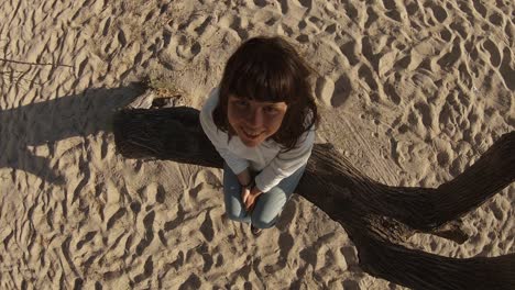 smiling cute young woman sits on tree trunk on beach, closeup overhead