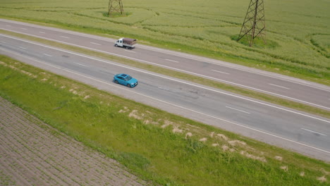 beautiful blue car driving on a highway. luxury electric automobile moving on a road on green fields background. slow motion. aerial view.