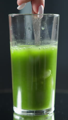 agua que se vierte en un vaso con jugo verde creando burbujas y un suave remolino