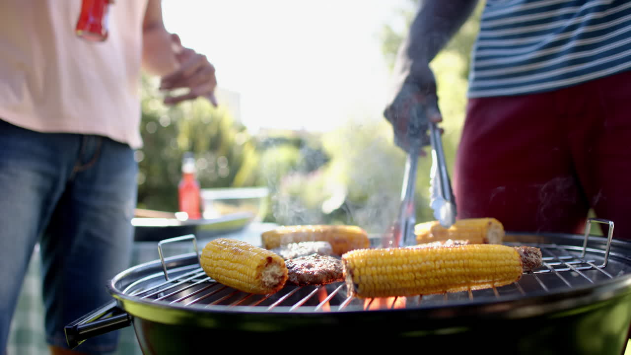 Grilling corn and meat on barbecue, two multiracial male friends enjoying outdoor hangout