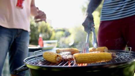 grilling corn and meat on barbecue, two multiracial male friends enjoying outdoor hangout