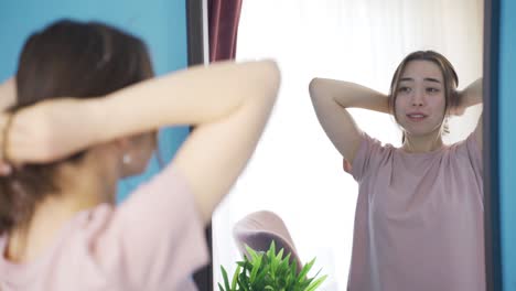 Happy-asian-young-woman-tying-her-hair-in-front-of-mirror.