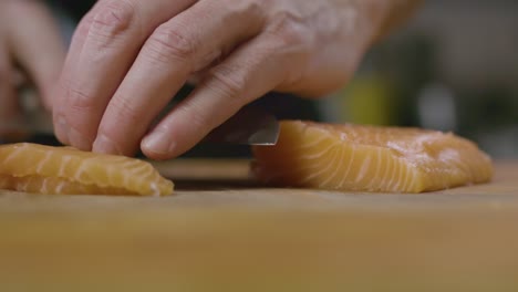 close up chef´s hand, slice the raw salmon fish in wooden board, depth of field