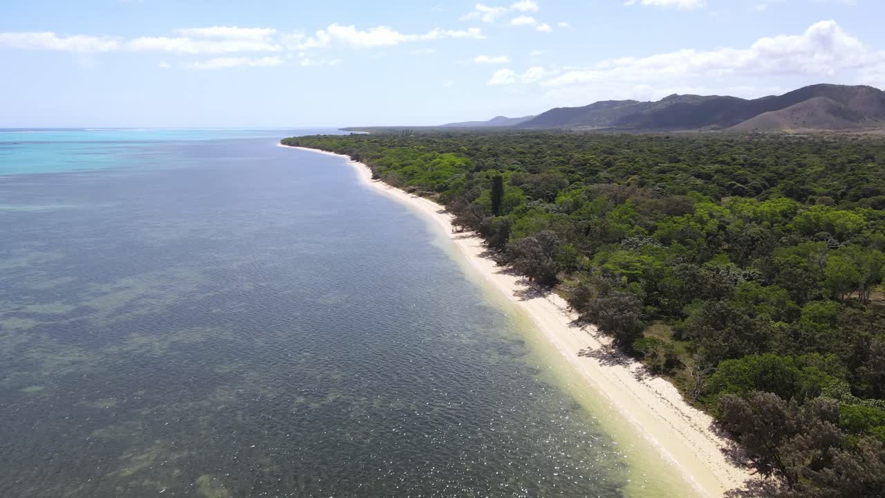 Drone aerial moving forward and panning over a beach with a mountainscape in New Caledonia
