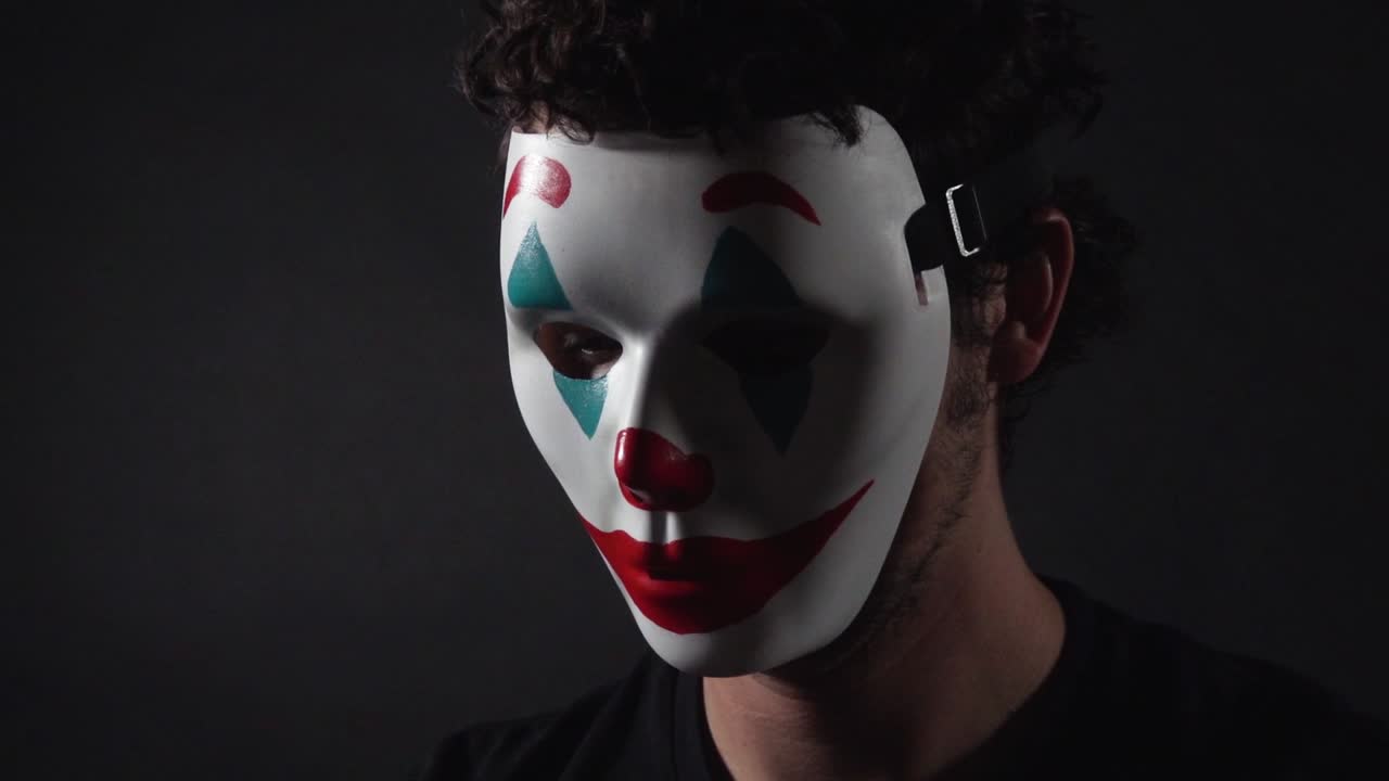 hombre que lleva la máscara de payaso con el tema del bromista en una habitación negra oscura