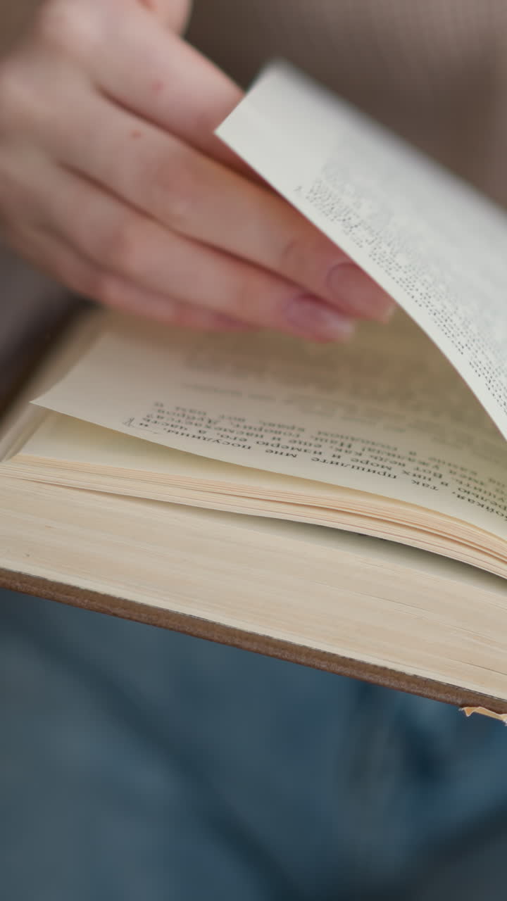 vista parcial de la mano de la mujer volviendo suavemente a través de un libro, mostrando la interacción táctil con las páginas en enfoque suave, con texto en las páginas visibles