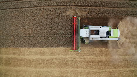 modern green harvester with red mower cuts the crops. top side view of a working machine moving along the ripe plantation.