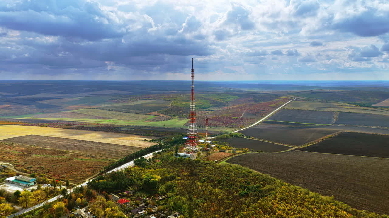 Aerial drone view of a tall radio transmission tower rising above Moldovan farmlands under a dramatic cloudy sky