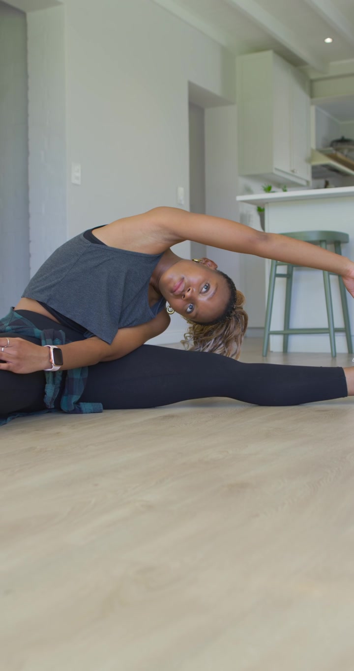 Vertical video: African American woman stretching side, reaching overhead on floor for mobility