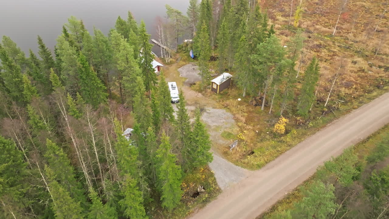 Una strada in una foresta di abeti con un camper parcheggiato sulla riva del lago in Svezia durante l'autunno
