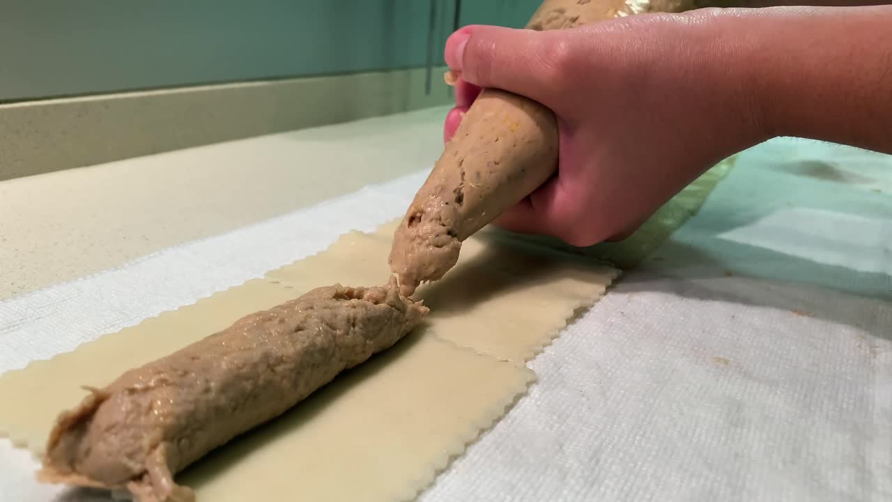 Young woman preparing handmade cannelloni. Stuffing cannelloni in a white kitchen. Cooking some fresh pasta.