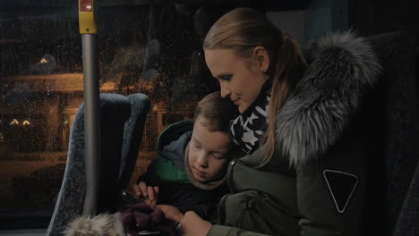 Mom-and-kid-playing-on-mobile-during-evening-bus-ride