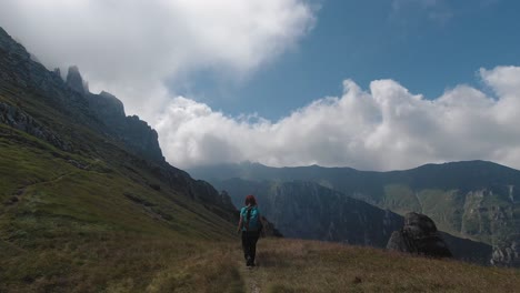 Follow-shot-of-a-girl-hiking-with-steep-mountain-ridges-in-the-background