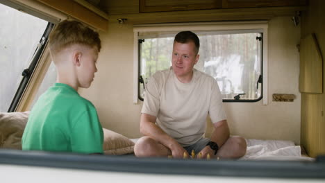 father and son playing chess sitting on the campervan bed