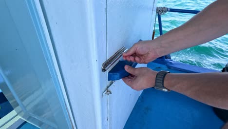 a person unlocks and opens a boat's engine room door on clear waters in phuket, thailand. bright daylight enhances visibility