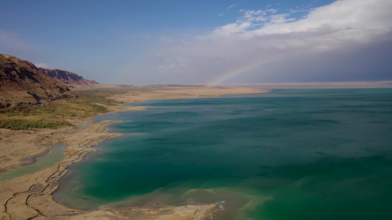 arco iris sobre el mar muerto de agua verde, cielo medio nublado, disparo de dron volador hacia adelante