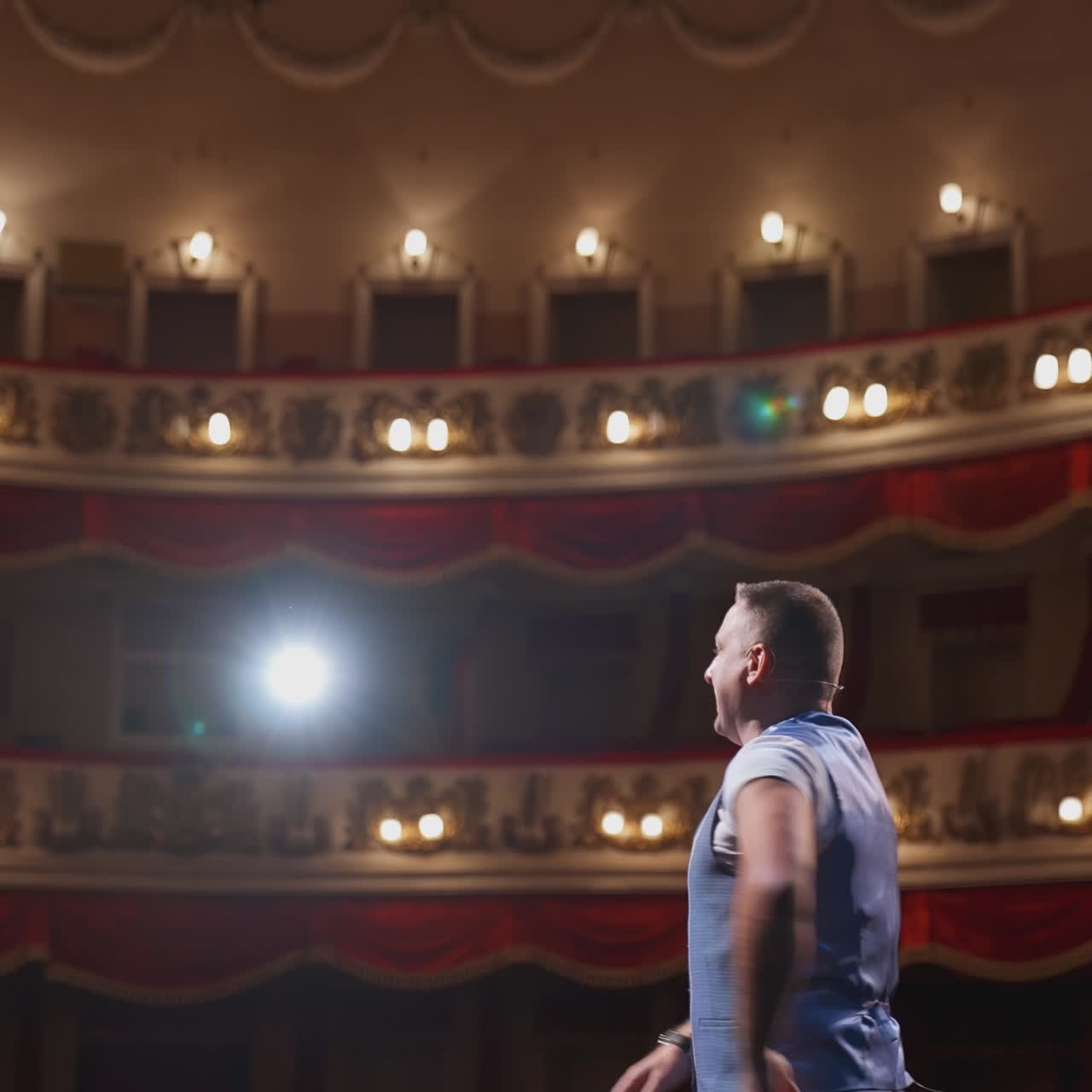 Comedian speaking jokes on stage. Actor standing on scene in spotlights with his back to the camera. Active man making gestures with his hands on a theatre stage.