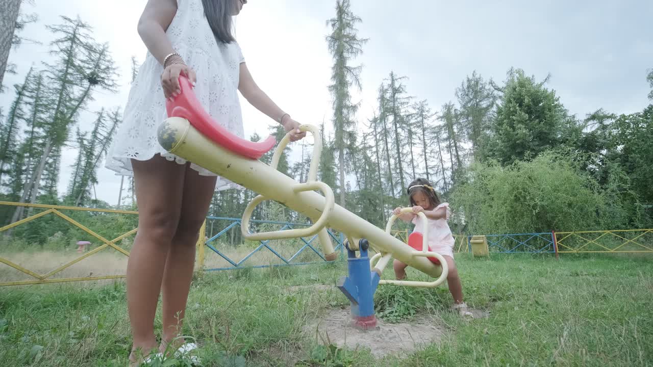 una madre embarazada y su hija joven disfrutan de un tiempo de juego juntos en un patio de recreo en el parque, rodeados de árboles y vegetación