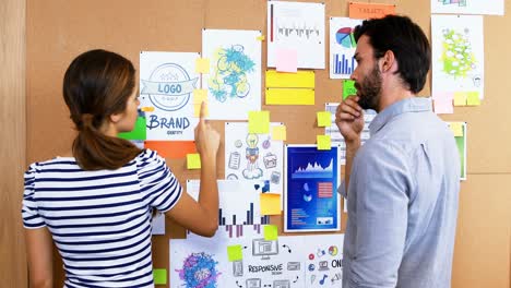 Male-and-female-executives-discussing-over-bulletin-board