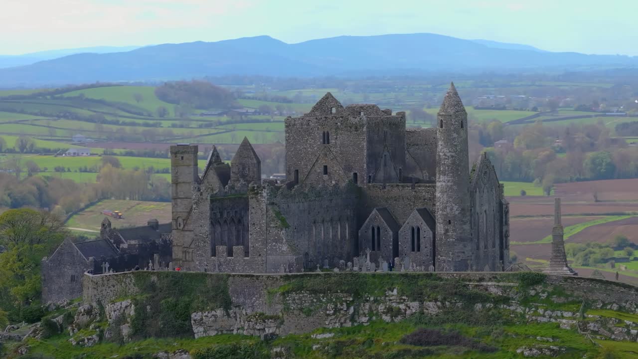 4K Aerial view of the Rock of Cashel, capturing ancient stone walls, round towers, and cathedral ruins surrounded by rolling green fields and historic farmland. Co.Tipperary, Ireland_05