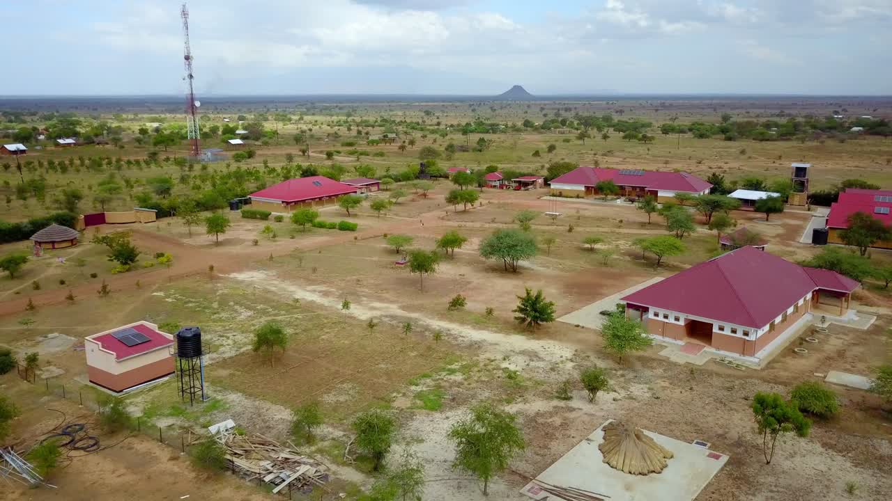 Aerial establishing shot capturing a vocational school in Karamoja, Uganda, featuring red-roofed buildings, solar panels, and water tanks amid a dry landscape, showcasing sustainable infrastructure
