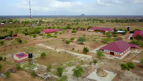 aerial establishing shot capturing a vocational school in karamoja, uganda, featuring red-roofed buildings, solar panels, and water tanks amid a dry landscape, showcasing sustainable infrastructure