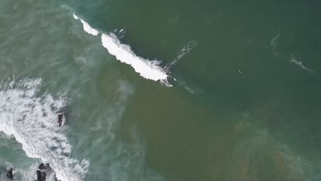 a drone rotates around an aerial view of surfers surfing and waves crashing