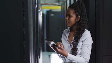 técnica informática afroamericana que usa una tableta trabajando en una sala de servidores de negocios
