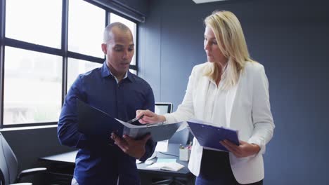 Diverse-business-colleagues-standing-talking-going-through-paperwork-in-modern-office