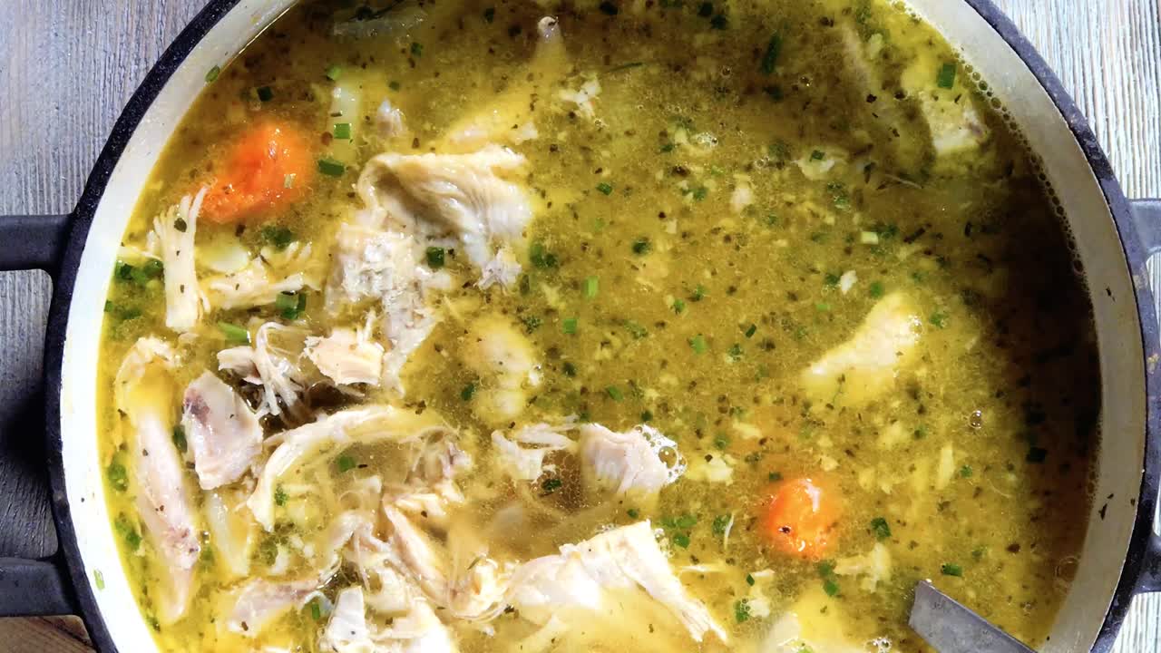 cucharón de primer plano superior revolviendo sopa de fideos de pollo casera con zanahorias en una olla grande