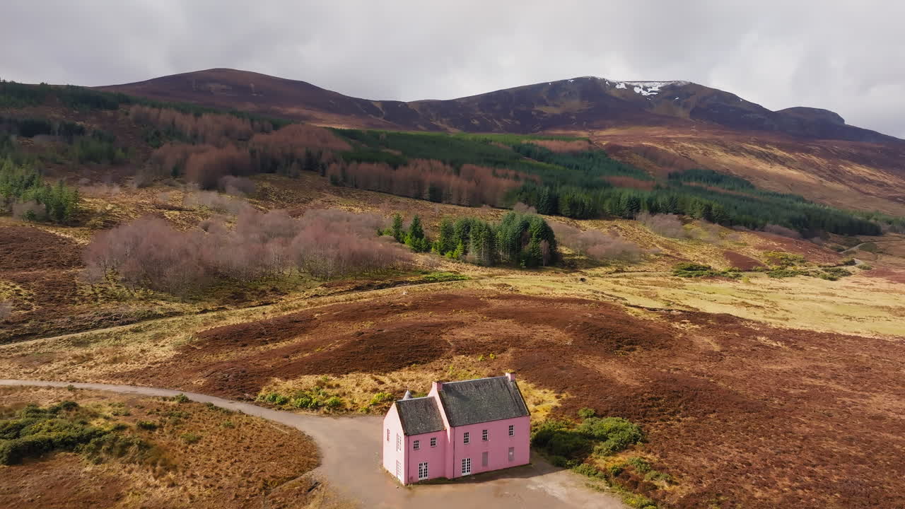 Small pink house stands alone near Loch Glass in Scottish Highlands, surrounded by rolling hills
