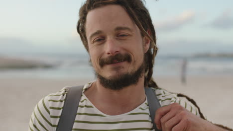 portrait of attractive carefree man with dreadlocks smiling at beach