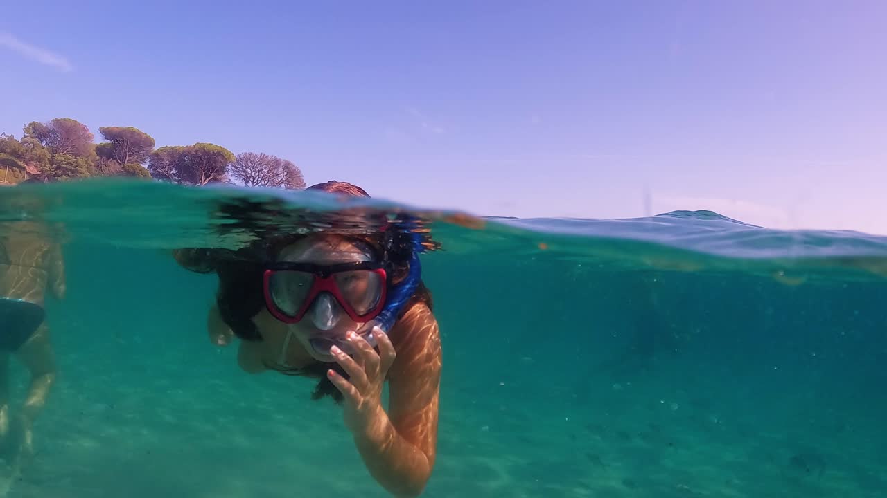 Halv undervandsscene af en lille pige med dykkermaske og snorkel, der svømmer i turkis tropisk havvand ved en eksotisk ø