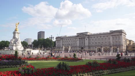 buckingham palace in london with walking people and red flowers in garden, wide angle shot, panning left