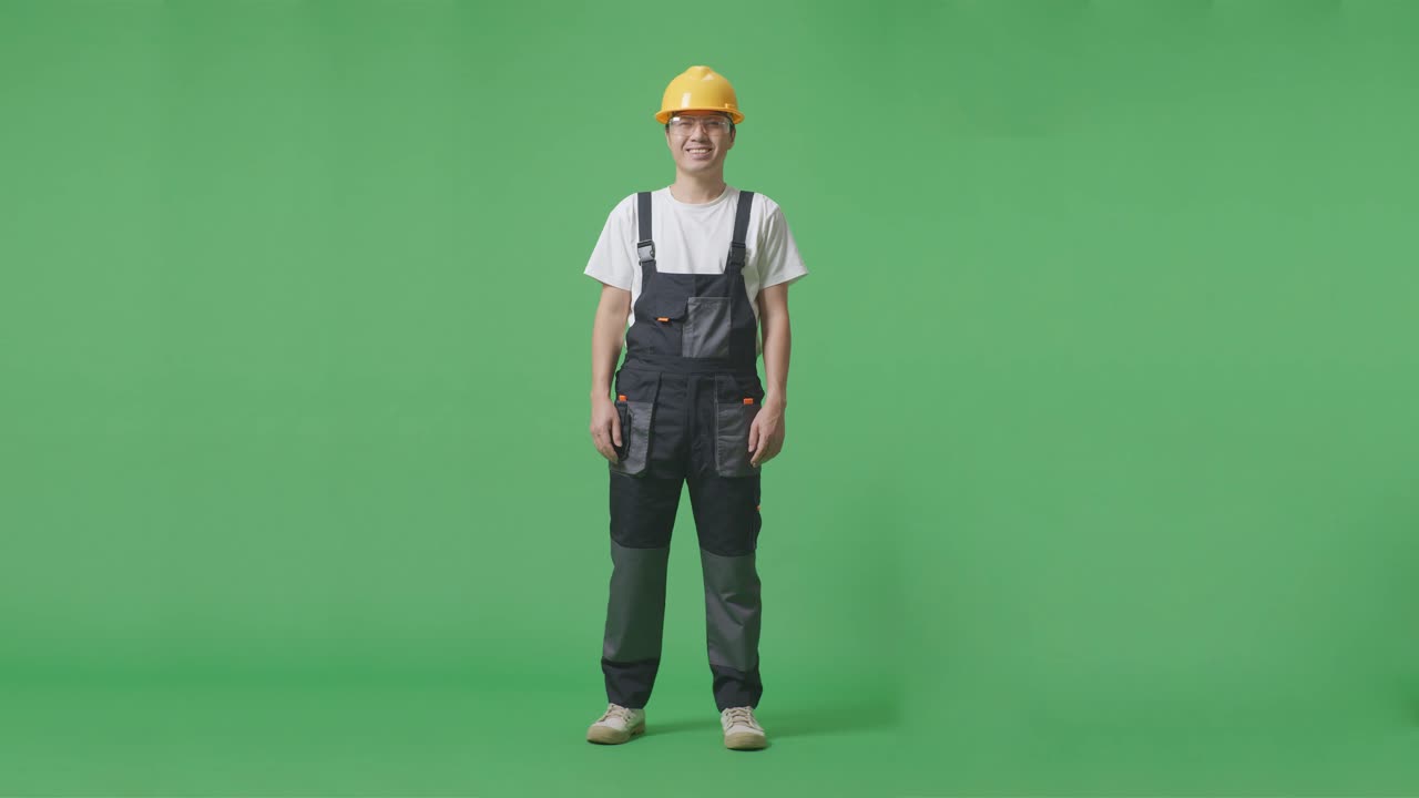 полное тело азиатского мужчины рабочий в защитных очках и защитном шлеме стоит и улыбается камере в зеленом экране фоновой студии