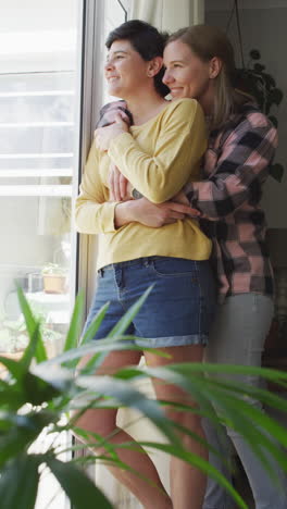 video vertical de una feliz pareja de lesbianas caucásicas abrazándose en casa