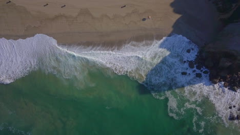 Aerial-drone-top-down-view-of-sea-waves-break-on-rock-and-sand