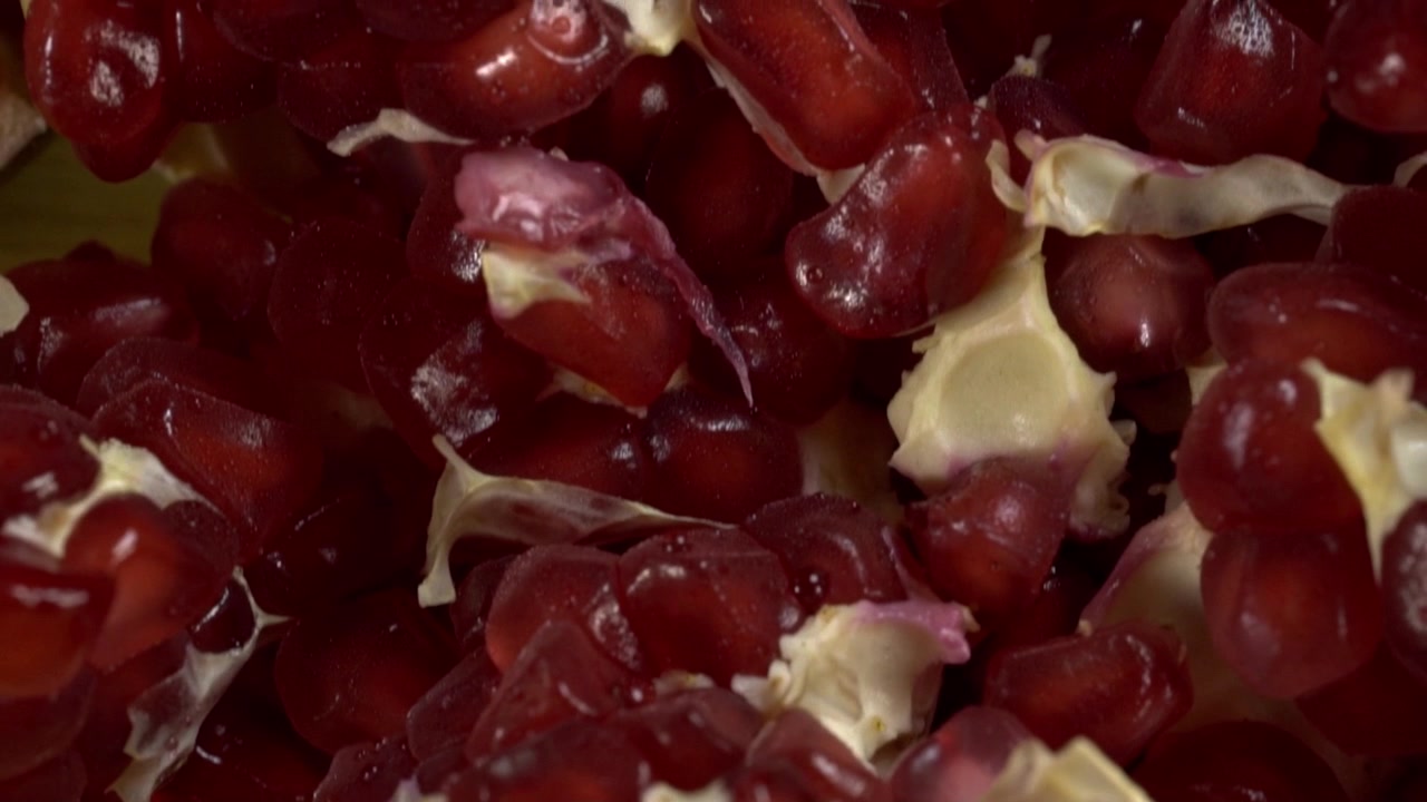 Primo piano di semi di melograno freschi con membrane chiare del frutto in dettaglio macro. Arilli rossi lucidi riempiono l'inquadratura, mostrando forme, texture e colori naturali vari