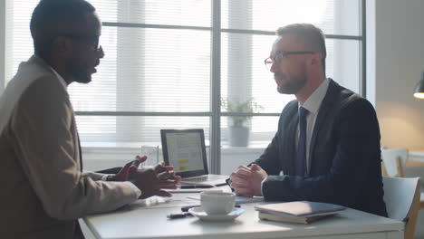 two multiethnic businessmen shaking hands and speaking in office