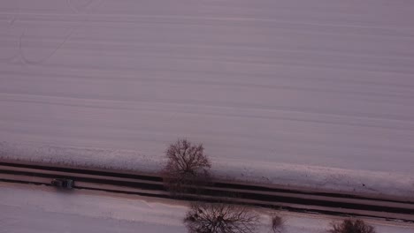 cars drive along not fully cleared of snow local road between snow-covered fields