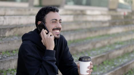 hombre sonriente con café para ir a hablar por teléfono inteligente