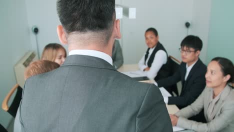 man with beard on face standing in front of his teammates presenting business strategy on meeting