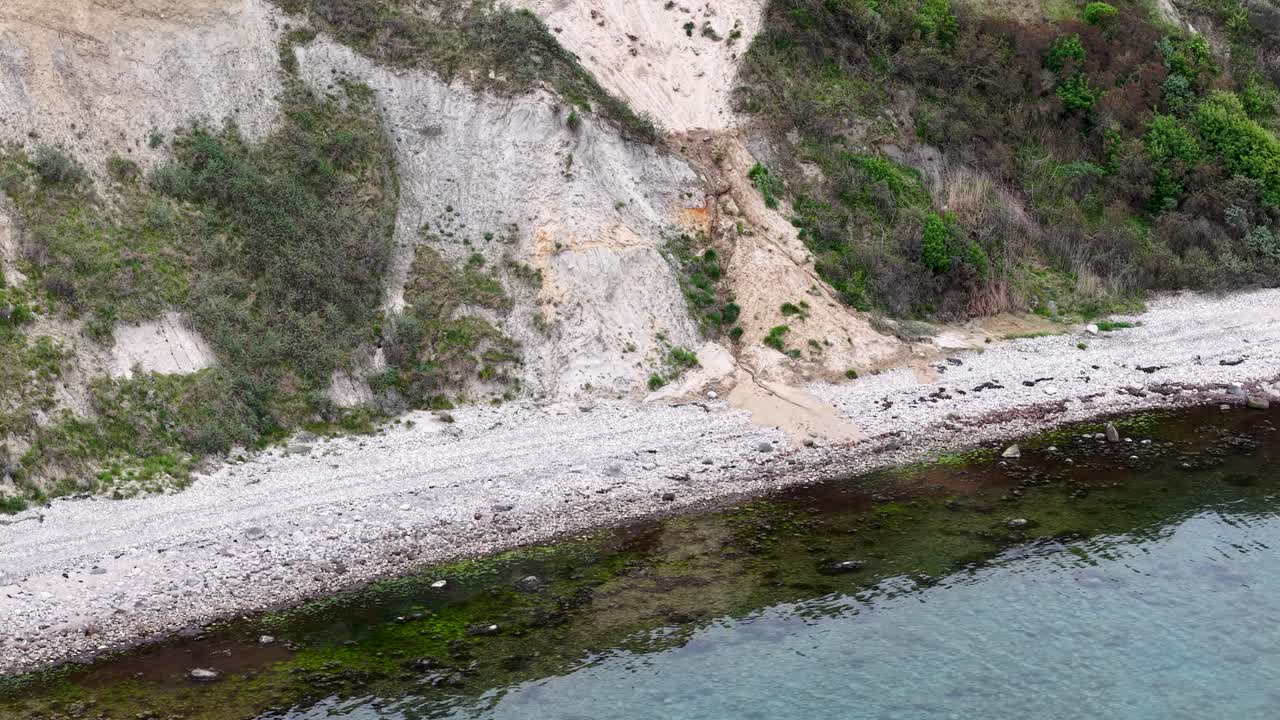 Drone shot of a steep white cliffside with a narrow path winding through green shrubs and brush