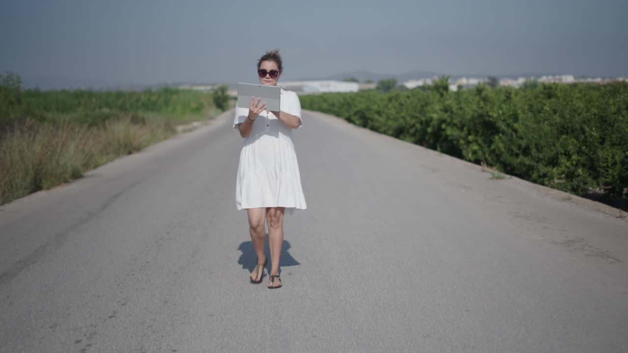Woman walking on a rural road with a tablet
