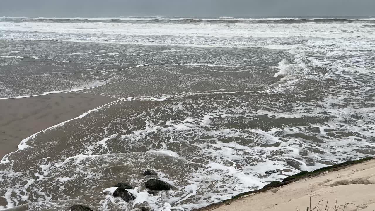Onde atlantiche che si infrangono da ogni angolazione su una spiaggia sabbiosa con un cielo invernale grigio. Portogallo