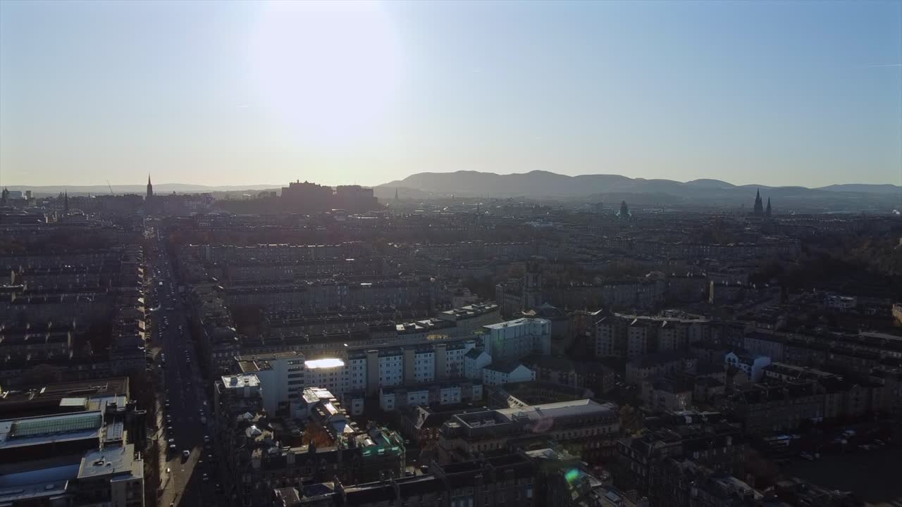 Drone footage of Edinburgh cityscape at sunset, featuring Edinburgh Castle, autumn colors, and distant hills. The clip captures historic streets, rooftops, and the city’s iconic landmarks in evening.