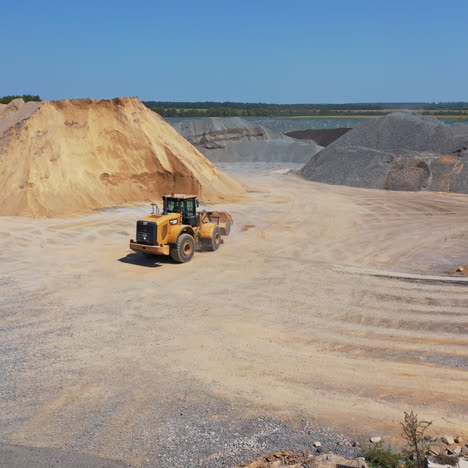 bulldozer transports sand in a bucket. asphalt plant surrounded by piles of crushed stones and gravel. industrial territory of a modern factory outdoors.